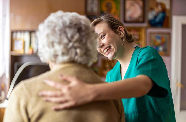 Two senior residents receiving medication from a caregiver in a comfortable, home-like common room.